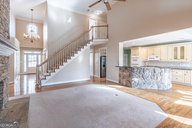 unfurnished living room featuring crown molding, a towering ceiling, ceiling fan with notable chandelier, and light hardwood / wood-style flooring