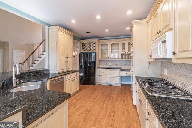 kitchen featuring appliances with stainless steel finishes, sink, decorative backsplash, dark stone counters, and light hardwood / wood-style floors