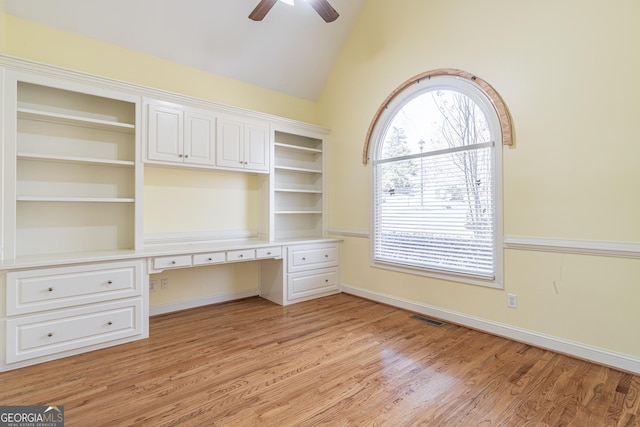 unfurnished office with ceiling fan, lofted ceiling, built in desk, and light hardwood / wood-style flooring