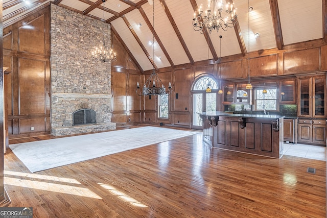 interior space featuring beam ceiling, a fireplace, light wood-type flooring, a chandelier, and wood walls