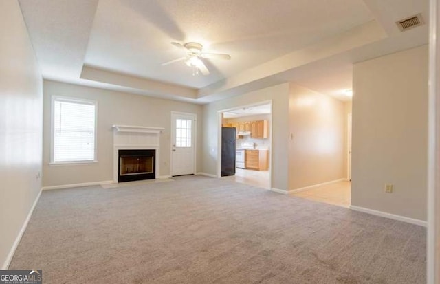 unfurnished living room featuring ceiling fan, a raised ceiling, and light carpet