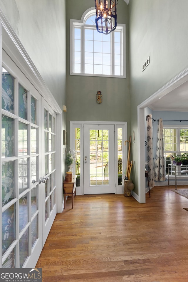 doorway with hardwood / wood-style flooring, a towering ceiling, a notable chandelier, and french doors