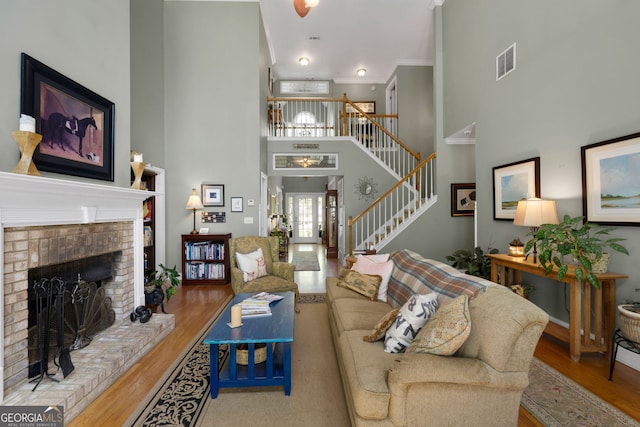 living room with crown molding, a towering ceiling, a brick fireplace, and light hardwood / wood-style flooring