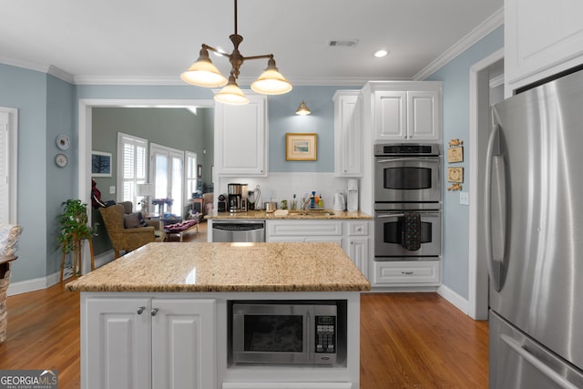 kitchen featuring white cabinets, hanging light fixtures, ornamental molding, a center island, and stainless steel appliances