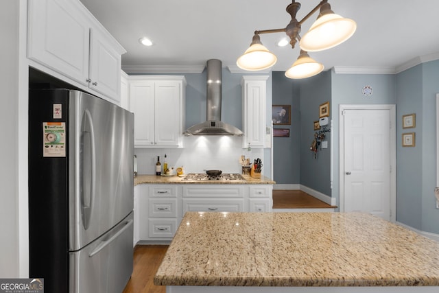 kitchen with white cabinets, stainless steel appliances, a center island, and wall chimney range hood