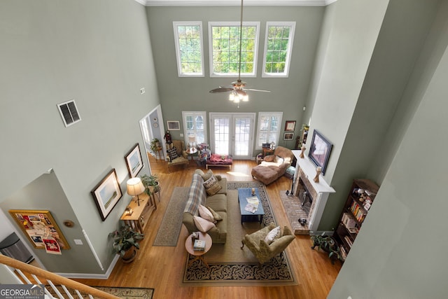 living room featuring a brick fireplace, a towering ceiling, light hardwood / wood-style flooring, and french doors