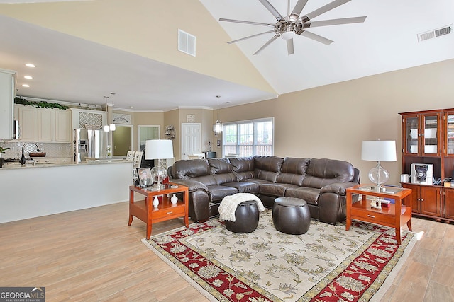 living room featuring high vaulted ceiling, sink, ornamental molding, ceiling fan, and light hardwood / wood-style flooring