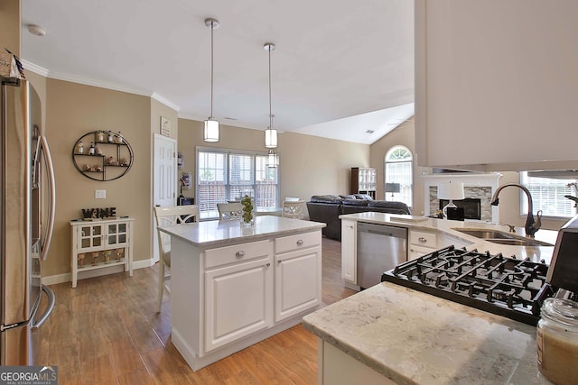 kitchen featuring a kitchen island, appliances with stainless steel finishes, a stone fireplace, sink, and white cabinets