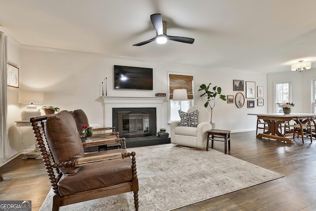 living room with a tile fireplace, crown molding, dark wood-type flooring, and ceiling fan