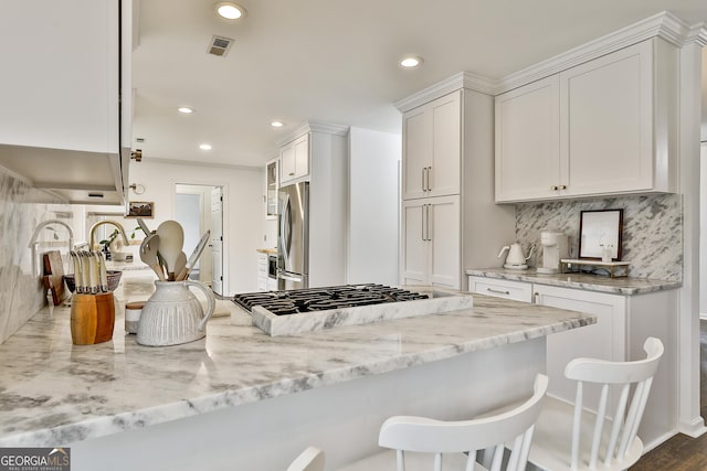 kitchen with a breakfast bar, white cabinetry, tasteful backsplash, stainless steel fridge, and light stone countertops