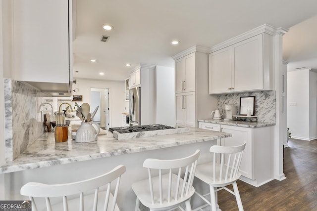 kitchen featuring stainless steel appliances, white cabinetry, a breakfast bar, and light stone counters