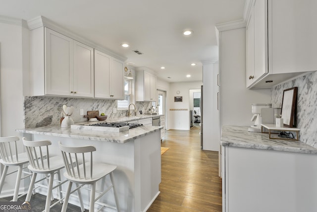 kitchen featuring a breakfast bar area, tasteful backsplash, light stone countertops, white cabinets, and dark hardwood / wood-style flooring