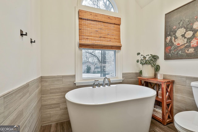 bathroom with wood-type flooring, toilet, a bath, and tile walls