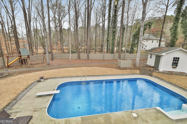 view of swimming pool with an outdoor structure, a diving board, and a playground