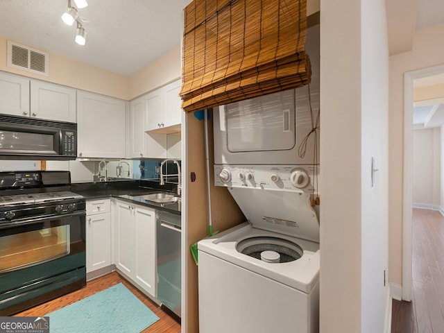 kitchen featuring white cabinetry, stacked washing maching and dryer, sink, and black appliances