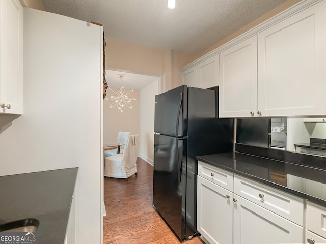 kitchen with hardwood / wood-style floors, an inviting chandelier, white cabinetry, dark stone counters, and a textured ceiling