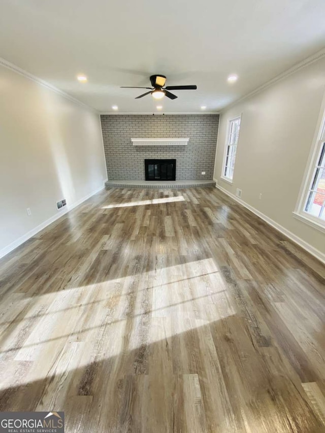 unfurnished living room with a fireplace, wood-type flooring, ornamental molding, and a healthy amount of sunlight