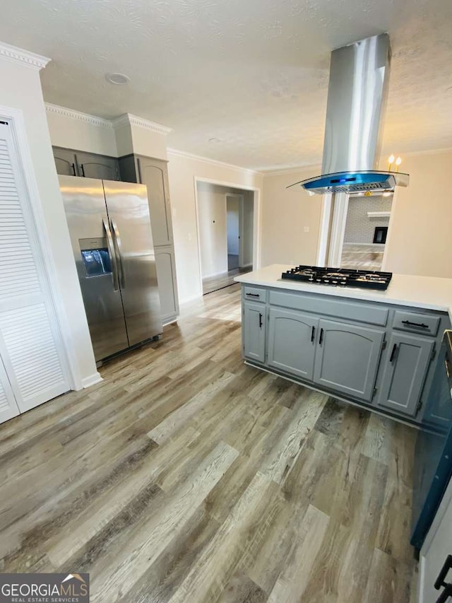 kitchen with stainless steel refrigerator with ice dispenser, ornamental molding, island range hood, and black gas stovetop