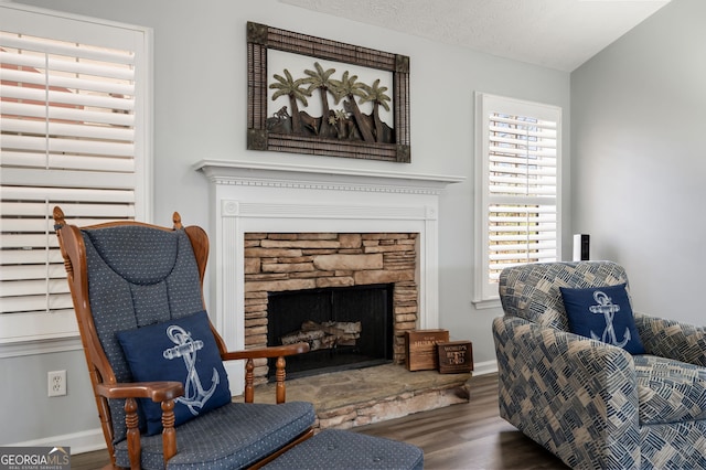 sitting room featuring wood-type flooring, a stone fireplace, and a textured ceiling