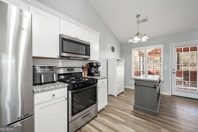 kitchen featuring vaulted ceiling, light hardwood / wood-style flooring, appliances with stainless steel finishes, decorative backsplash, and white cabinets