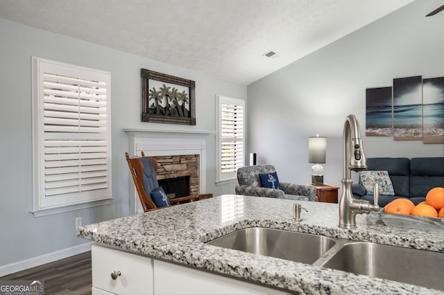 kitchen featuring vaulted ceiling, sink, white cabinets, light stone countertops, and dark wood-type flooring