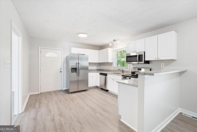 kitchen with sink, white cabinets, kitchen peninsula, stainless steel appliances, and light hardwood / wood-style flooring