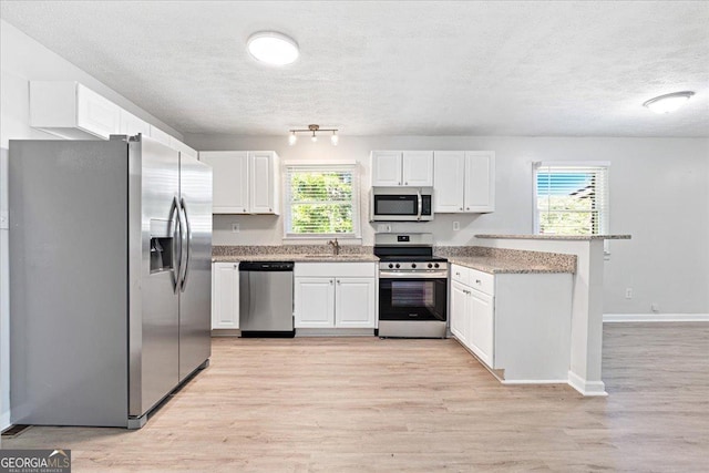 kitchen featuring stainless steel appliances, white cabinetry, a textured ceiling, and light wood-type flooring