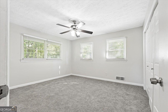 spare room with a textured ceiling, light colored carpet, and ceiling fan