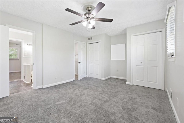 unfurnished bedroom featuring multiple closets, light carpet, a textured ceiling, and ensuite bath