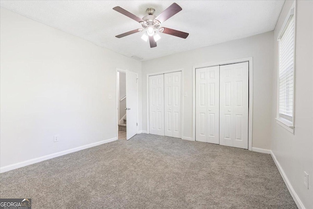 unfurnished bedroom with carpet floors, two closets, a textured ceiling, and ceiling fan