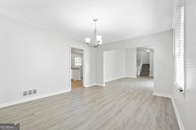 unfurnished living room featuring an inviting chandelier and light hardwood / wood-style floors