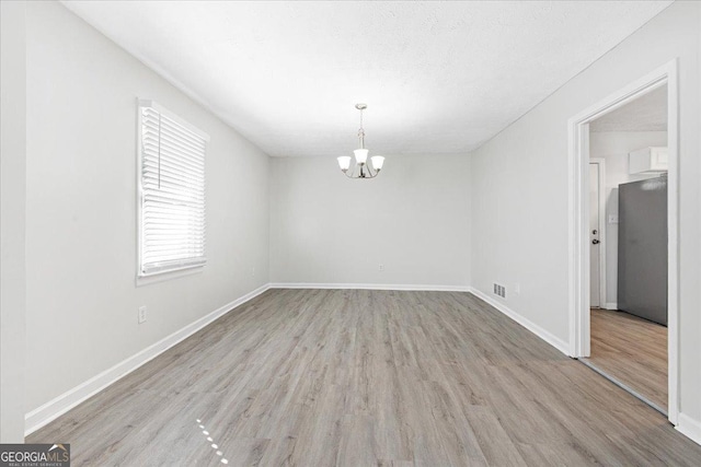 unfurnished room with a chandelier and light wood-type flooring