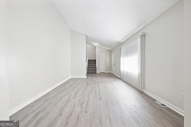 unfurnished living room with lofted ceiling, light hardwood / wood-style flooring, and a textured ceiling