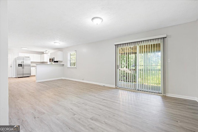 unfurnished living room featuring a textured ceiling and light hardwood / wood-style floors