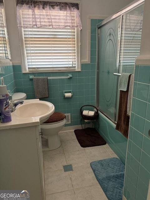 full bathroom with toilet, tile patterned floors, shower / bath combination with glass door, and tile walls