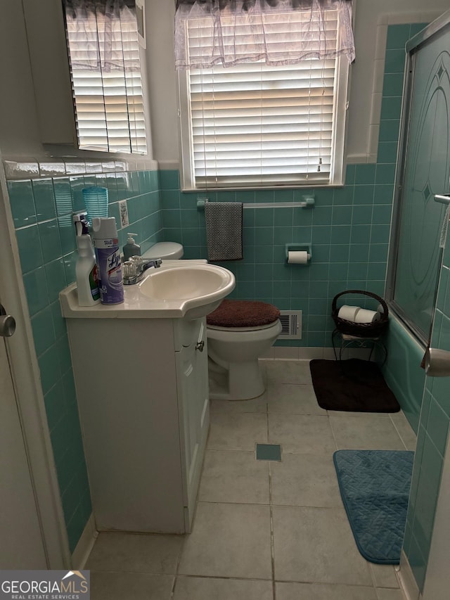 full bathroom featuring shower / bath combination with glass door, tile walls, vanity, tile patterned floors, and toilet