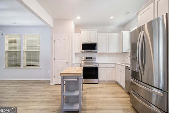 kitchen with appliances with stainless steel finishes, sink, white cabinets, backsplash, and light wood-type flooring