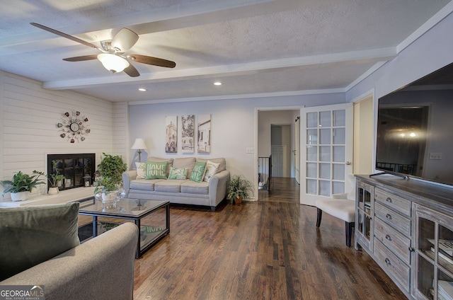 living room with ceiling fan, a large fireplace, a textured ceiling, dark hardwood / wood-style flooring, and beamed ceiling