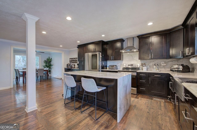 kitchen with a center island, appliances with stainless steel finishes, light stone countertops, decorative backsplash, and wall chimney range hood