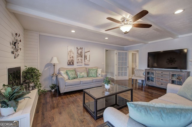 living room with dark hardwood / wood-style flooring, ceiling fan, a large fireplace, and beamed ceiling