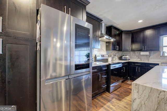 kitchen with stainless steel appliances, light stone countertops, light hardwood / wood-style floors, decorative backsplash, and wall chimney exhaust hood