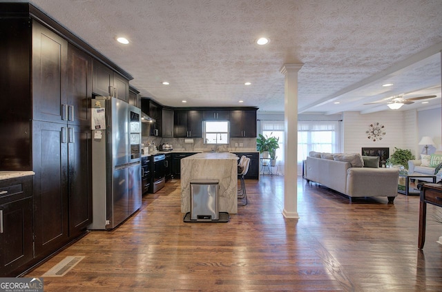 kitchen featuring ornate columns, dark hardwood / wood-style flooring, a kitchen island, and stainless steel refrigerator