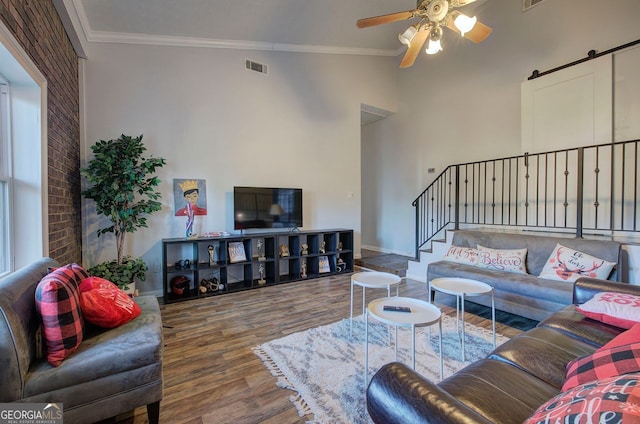 living room with crown molding, ceiling fan, a barn door, and hardwood / wood-style floors