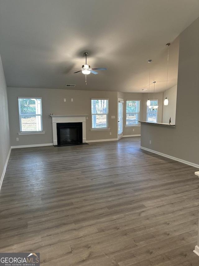 unfurnished living room featuring ceiling fan with notable chandelier, a wealth of natural light, and dark hardwood / wood-style floors