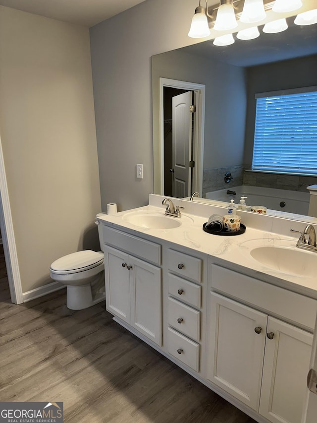 bathroom with hardwood / wood-style flooring, vanity, a notable chandelier, a tub, and toilet