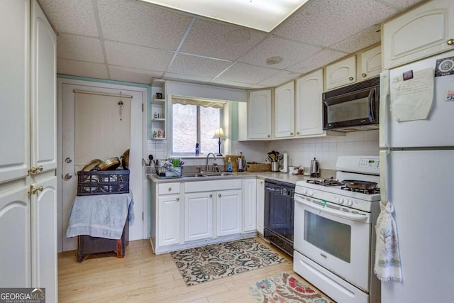 kitchen with a paneled ceiling, tasteful backsplash, sink, black appliances, and light wood-type flooring