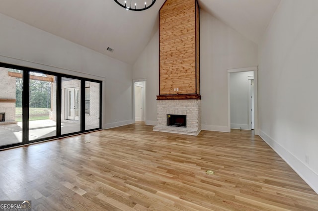 unfurnished living room with light hardwood / wood-style flooring, a fireplace, high vaulted ceiling, and a chandelier