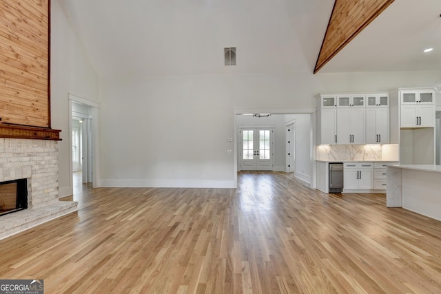 unfurnished living room with high vaulted ceiling, light hardwood / wood-style flooring, a fireplace, and french doors