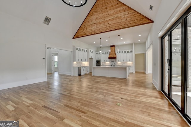 unfurnished living room with an inviting chandelier, high vaulted ceiling, and light hardwood / wood-style floors