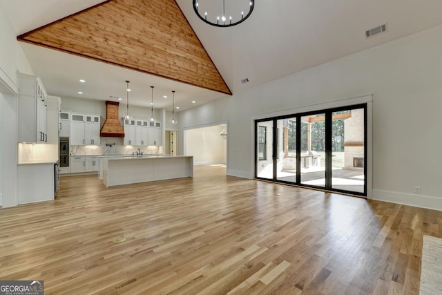 unfurnished living room with a notable chandelier, high vaulted ceiling, and light hardwood / wood-style flooring